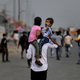 An Indian man carries his children on his shoulders as he along with his family walk along an expressway hoping to reach their home, hundreds of miles away, as the city comes under lockdown in Ghaziabad.